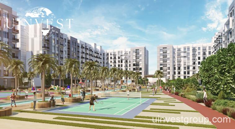 Exterior rendering of Lawnz by Danube Properties in Dubai International City, showing four eight-storey, country-themed freehold apartment buildings with pastel facades, geometric motifs, private balconies, surrounded by landscaped gardens, a community swimming pool, outdoor sports courts, and palm trees under a bright blue sky.