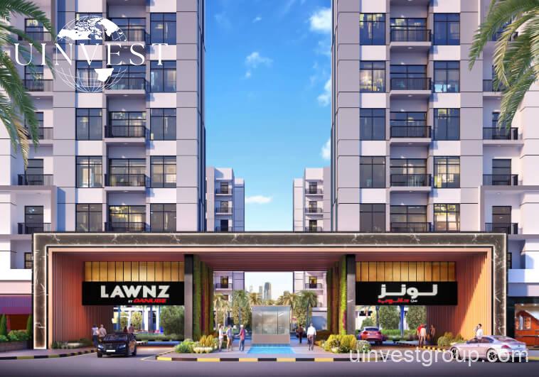 Exterior rendering of Lawnz by Danube Properties in Dubai International City, showing four eight-storey, country-themed freehold apartment buildings with pastel facades, geometric motifs, private balconies, surrounded by landscaped gardens, a community swimming pool, outdoor sports courts, and palm trees under a bright blue sky.