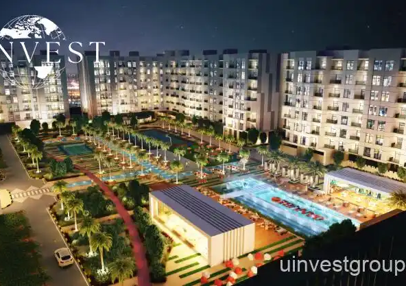 Exterior rendering of Lawnz by Danube Properties in Dubai International City, showing four eight-storey, country-themed freehold apartment buildings with pastel facades, geometric motifs, private balconies, surrounded by landscaped gardens, a community swimming pool, outdoor sports courts, and palm trees under a bright blue sky.