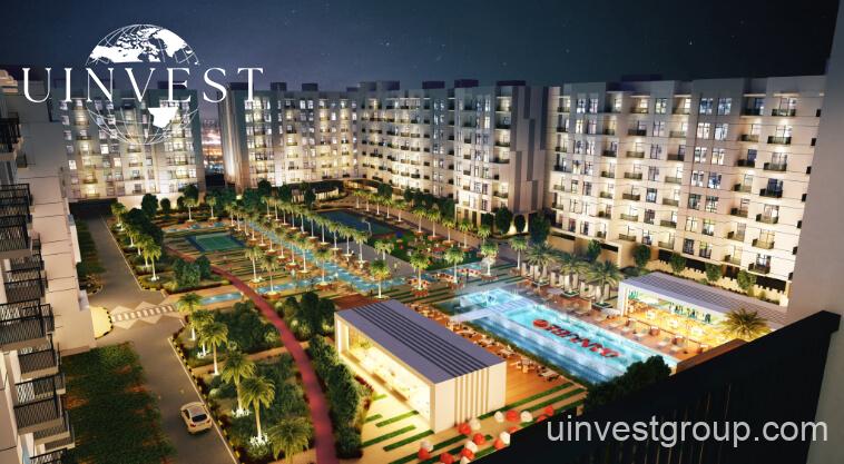 Exterior rendering of Lawnz by Danube Properties in Dubai International City, showing four eight-storey, country-themed freehold apartment buildings with pastel facades, geometric motifs, private balconies, surrounded by landscaped gardens, a community swimming pool, outdoor sports courts, and palm trees under a bright blue sky.