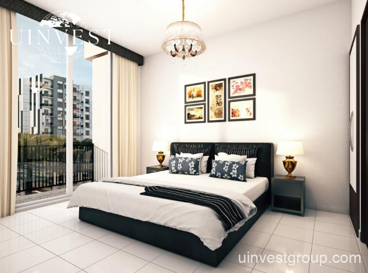 Exterior rendering of Lawnz by Danube Properties in Dubai International City, showing four eight-storey, country-themed freehold apartment buildings with pastel facades, geometric motifs, private balconies, surrounded by landscaped gardens, a community swimming pool, outdoor sports courts, and palm trees under a bright blue sky.