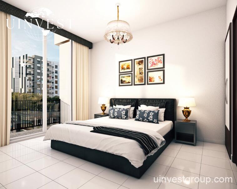 Exterior rendering of Lawnz by Danube Properties in Dubai International City, showing four eight-storey, country-themed freehold apartment buildings with pastel facades, geometric motifs, private balconies, surrounded by landscaped gardens, a community swimming pool, outdoor sports courts, and palm trees under a bright blue sky.
