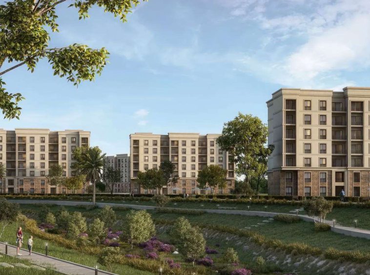 Sandstone-toned apartment buildings at Jood facing landscaped parkland in Sultan Haitham City, Muscat.