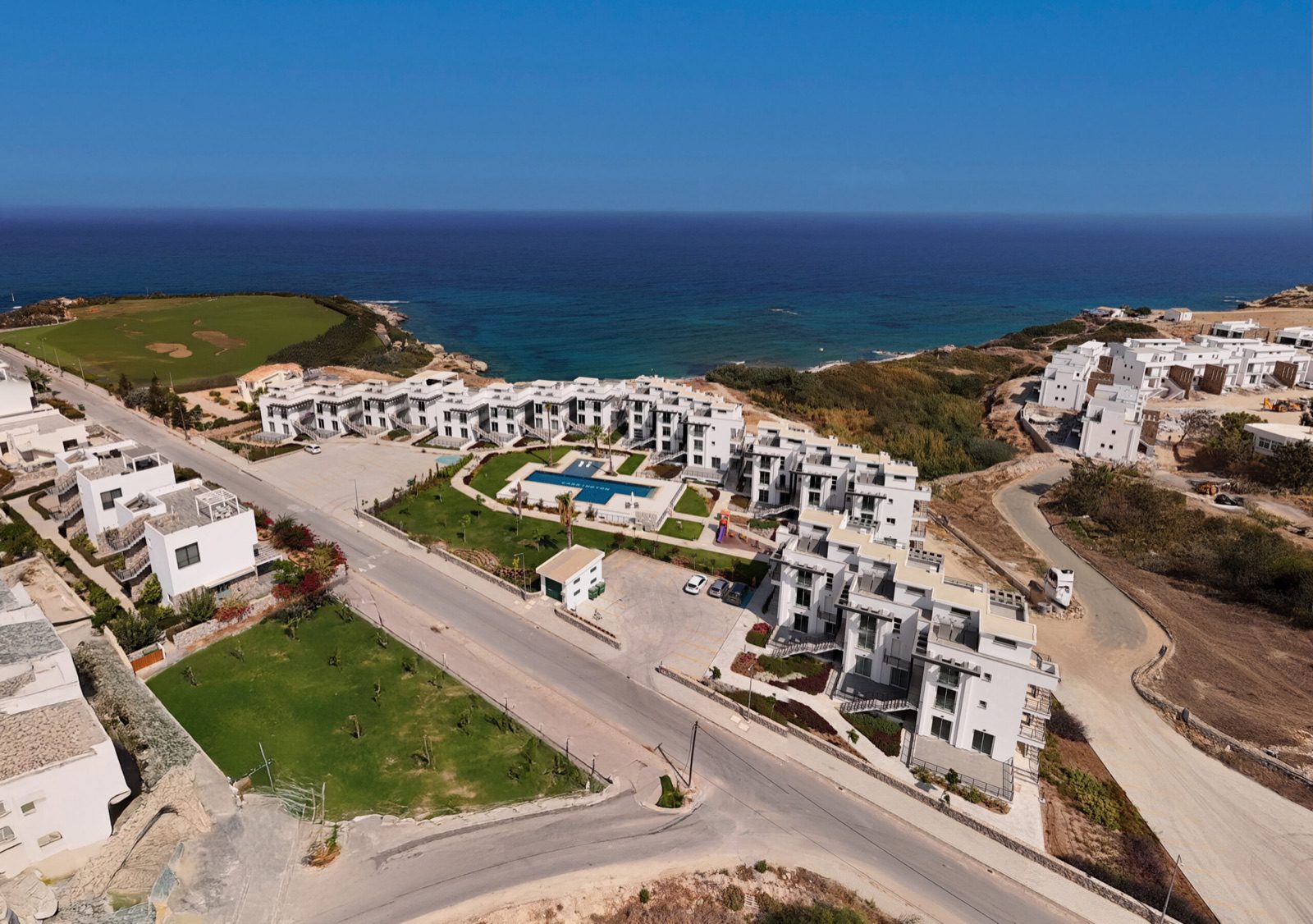 Aerial photo: apartment blocks, pool and access road with the sea behind