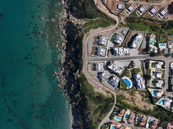 Top-down aerial photo of a bay beside an estate of white buildings with pools