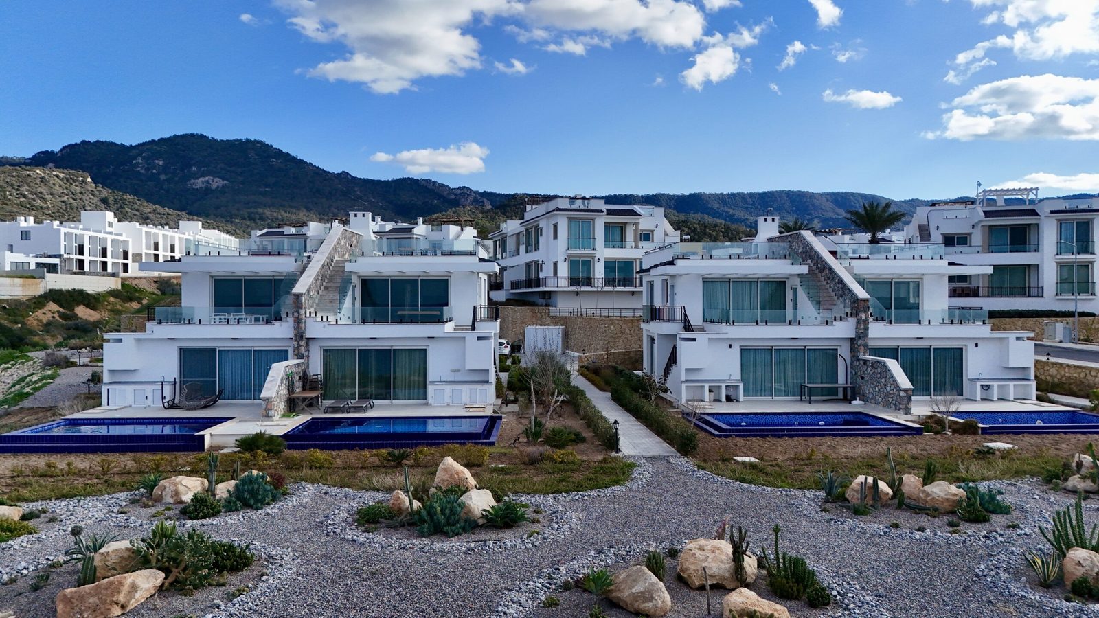 Photo of white modern houses with terraces and pools in front of a mountain backdrop