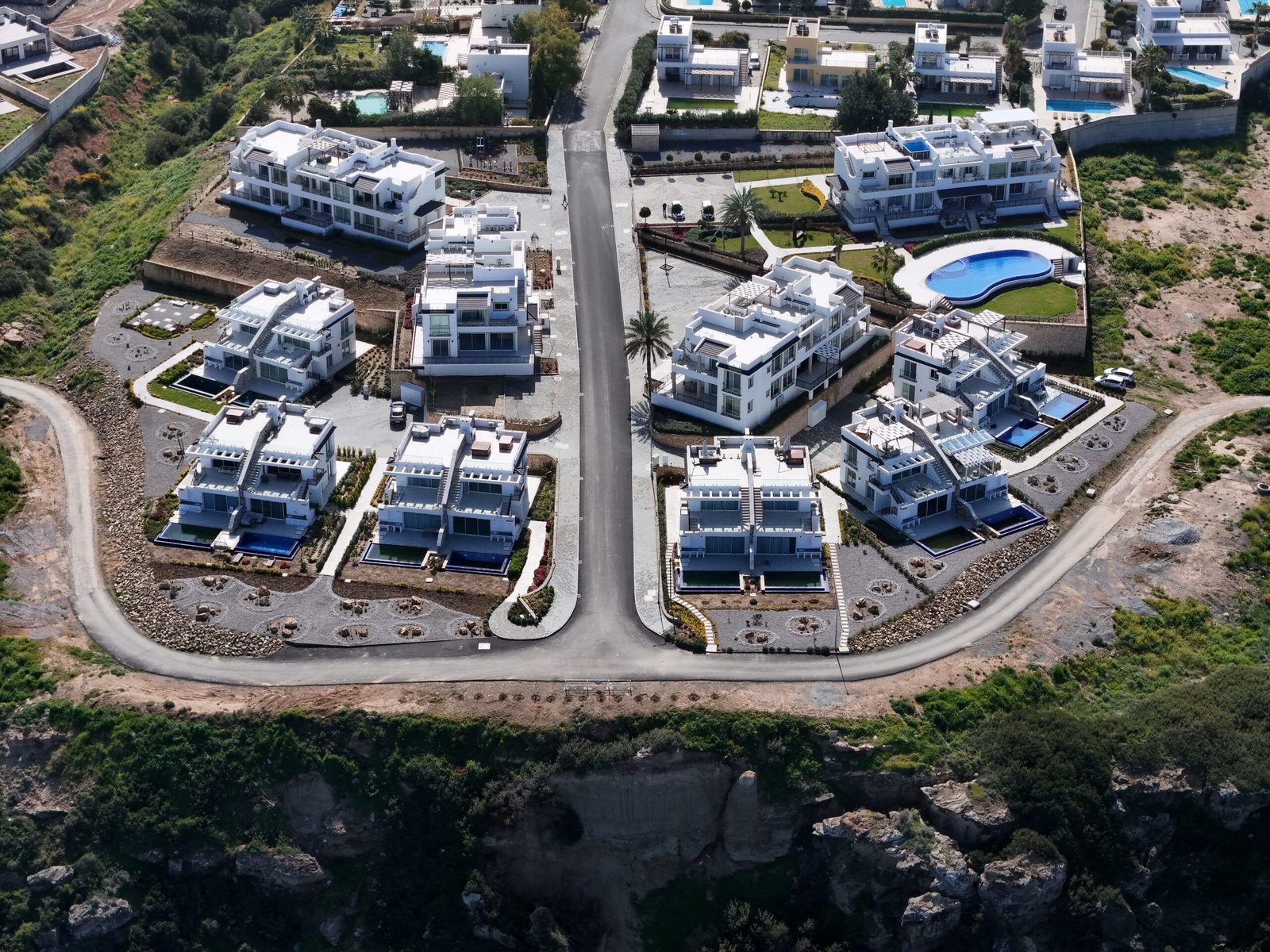Aerial photo of white buildings with pools along roads on a cliff-top plot