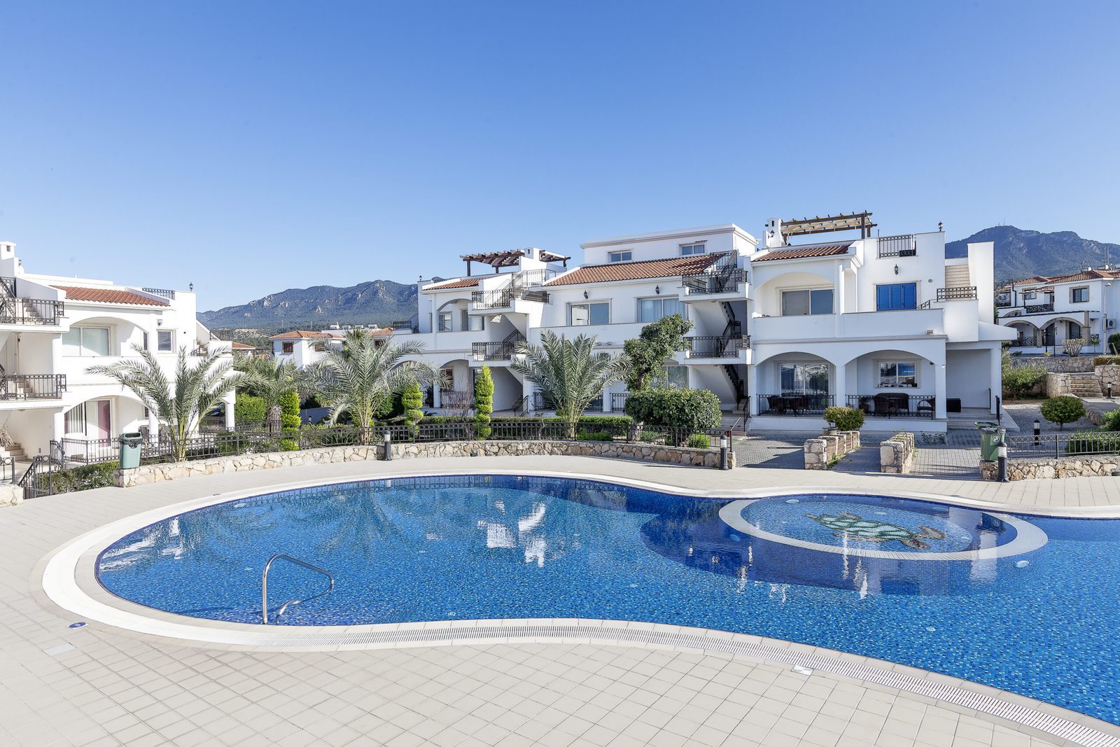 Photo of a free-form swimming pool with white apartment buildings and mountains behind