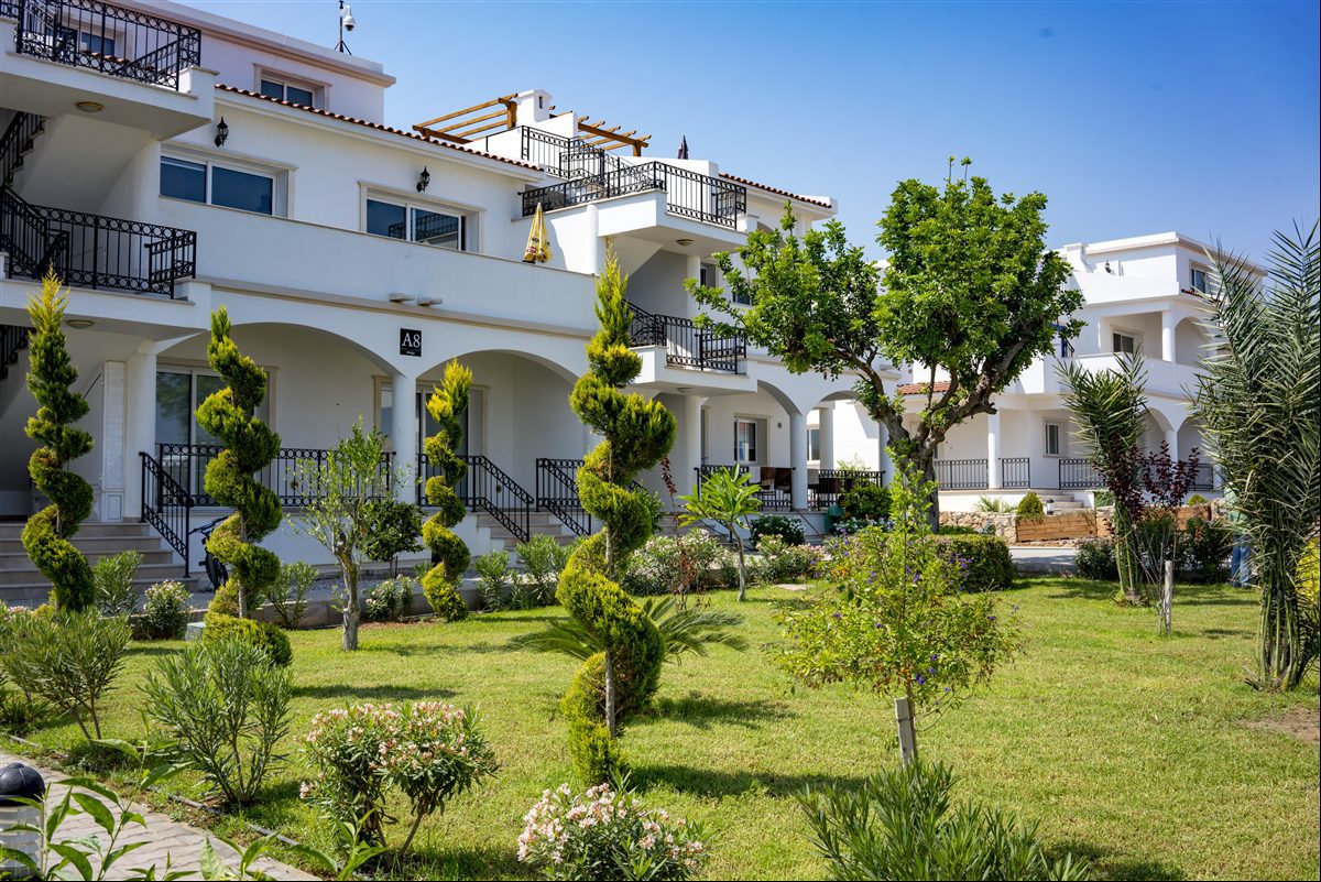 White apartment block with arcades and landscaped garden in the foreground