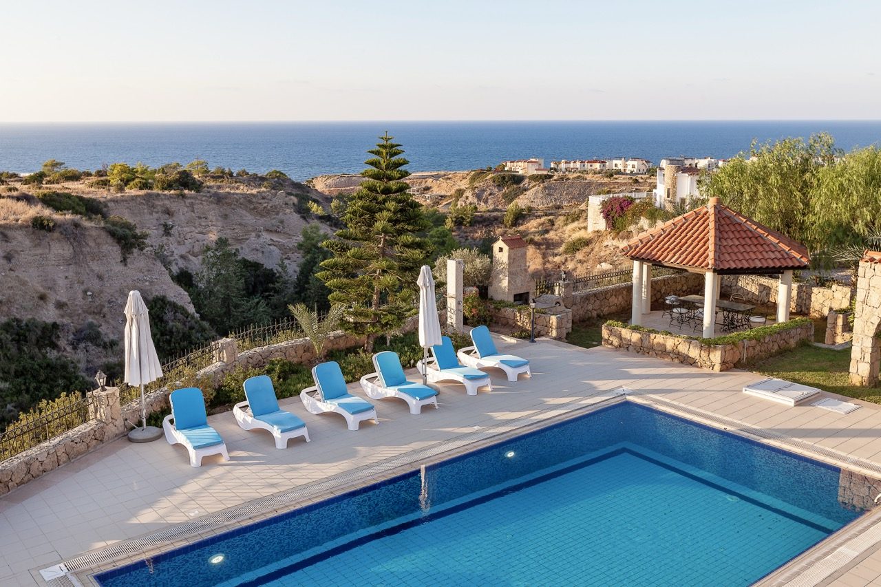 Villa swimming pool with sun loungers, a pergola and the sea in the distance