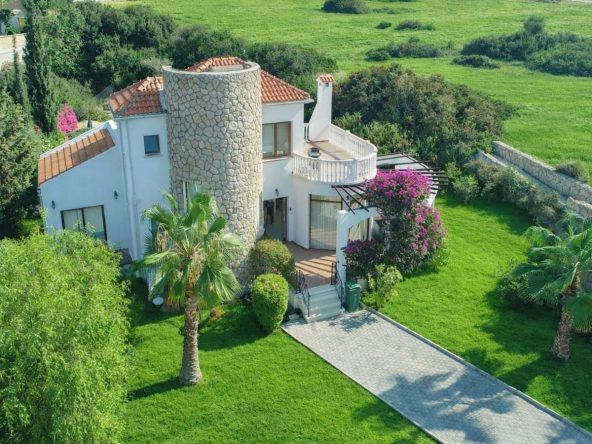 Aerial view of a white villa with a round stone tower and garden