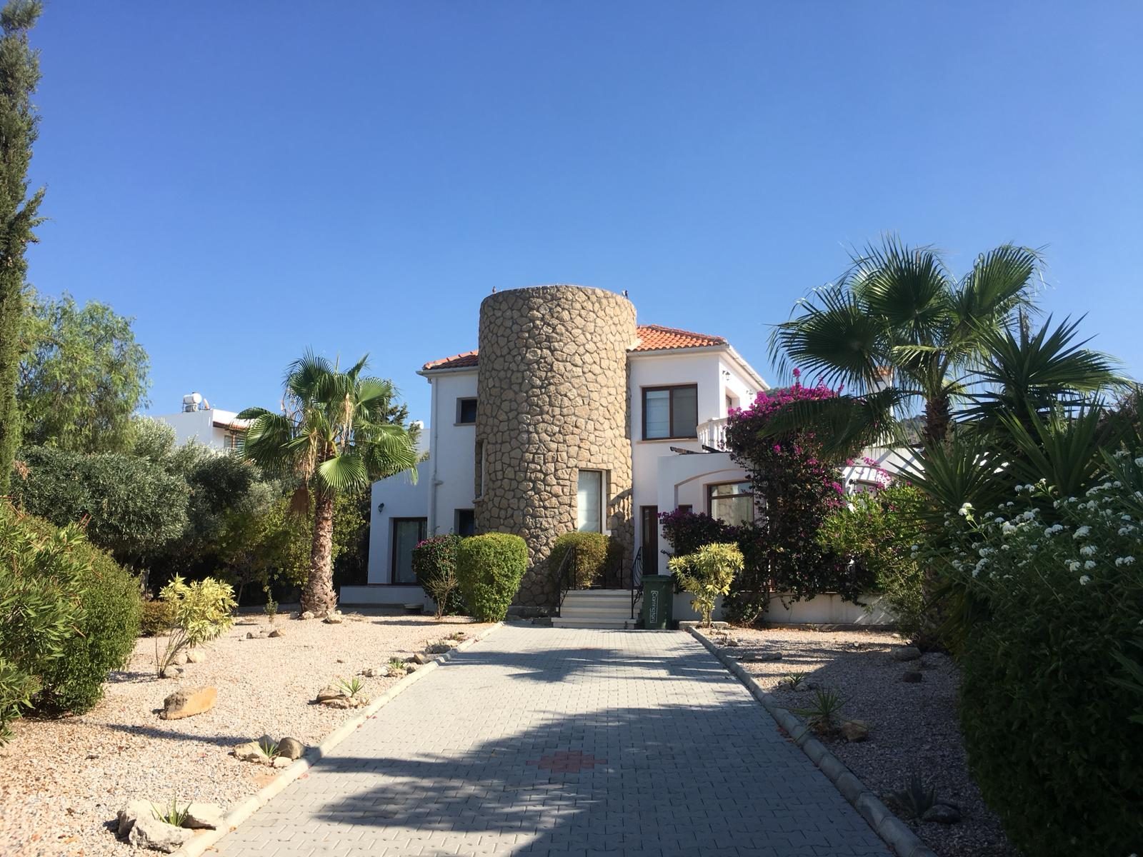Villa with a round stone tower at the end of a paved driveway