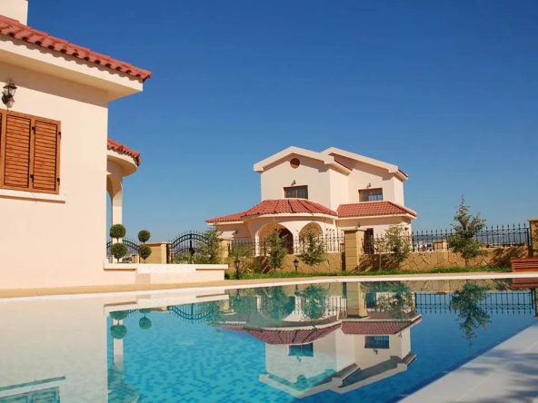 Swimming pool in front of a row of detached villas with tiled roofs