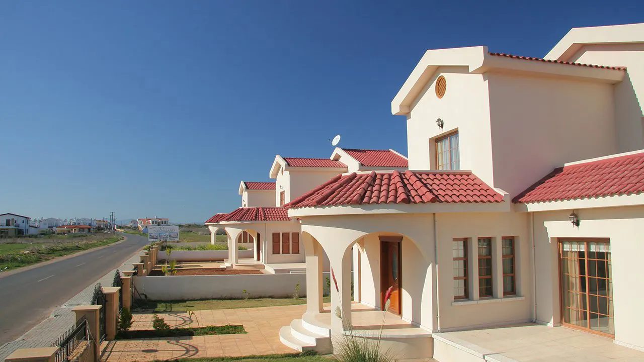 Row of detached villas with arched entrances and red tiled roofs beside a road