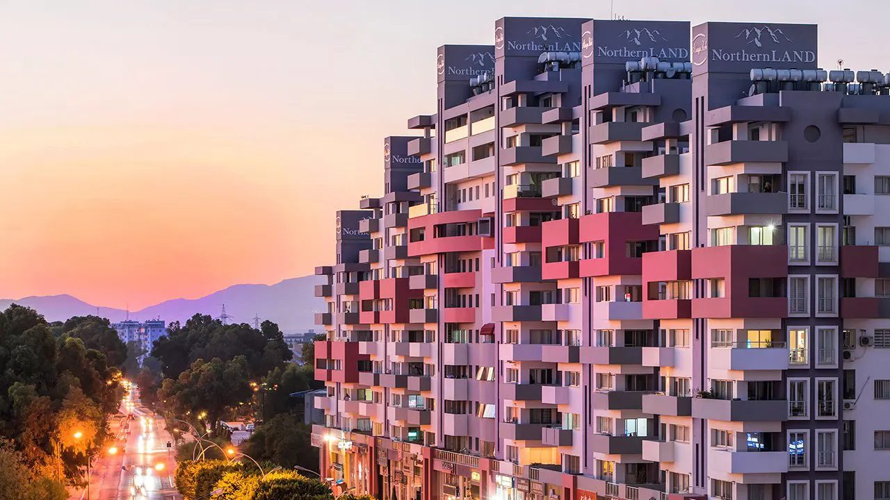 Apartment block at sunset with mountains behind and a lit street below