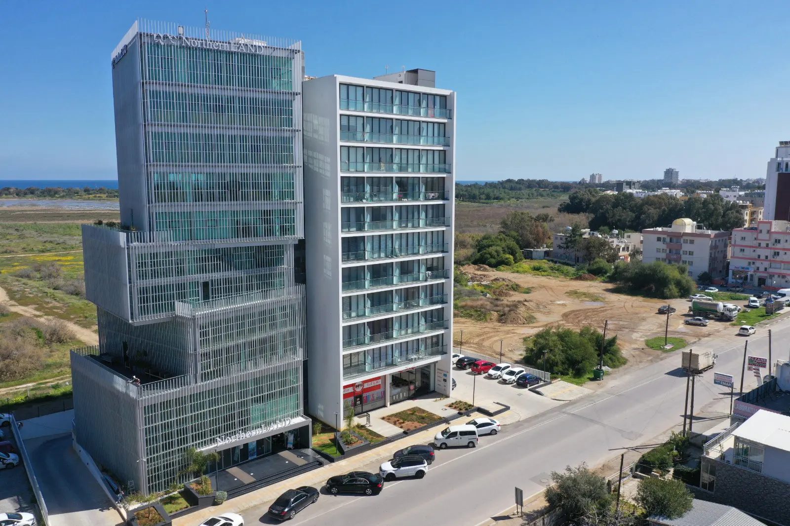 Aerial view of two glass towers beside a road with sea in the distance