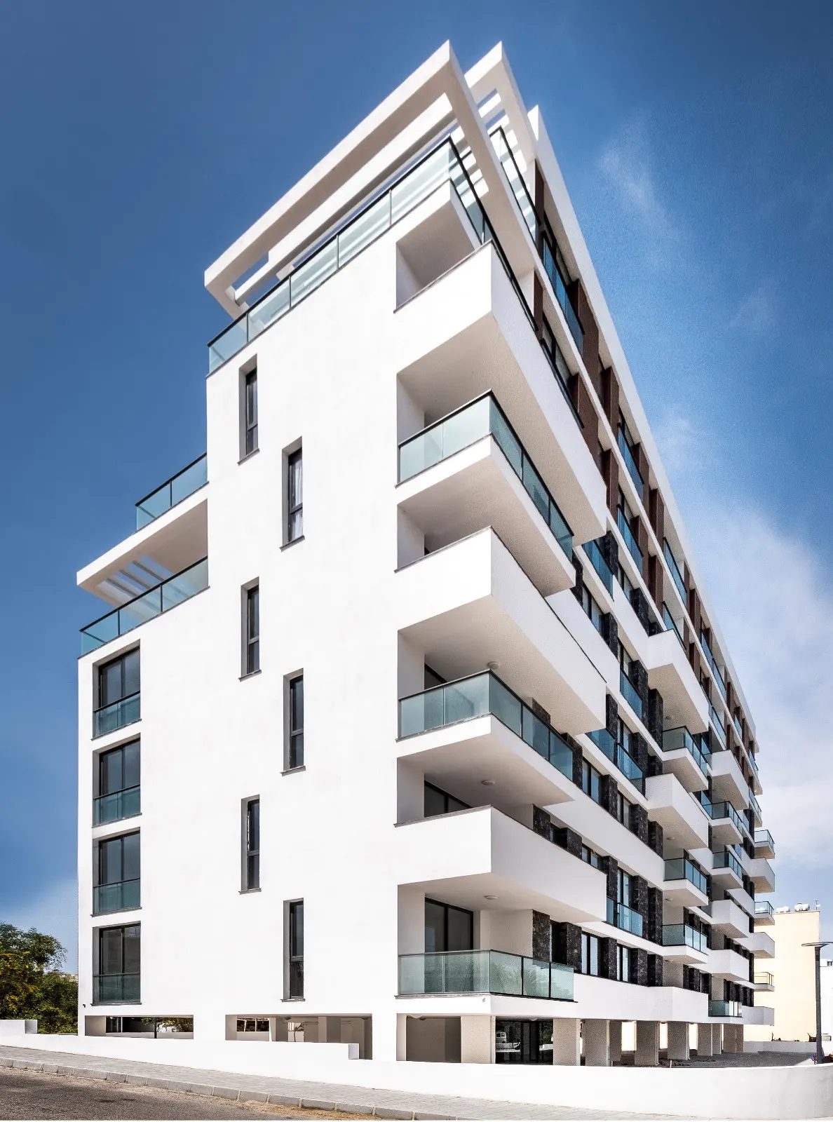 White apartment tower with glazed balconies against a blue sky