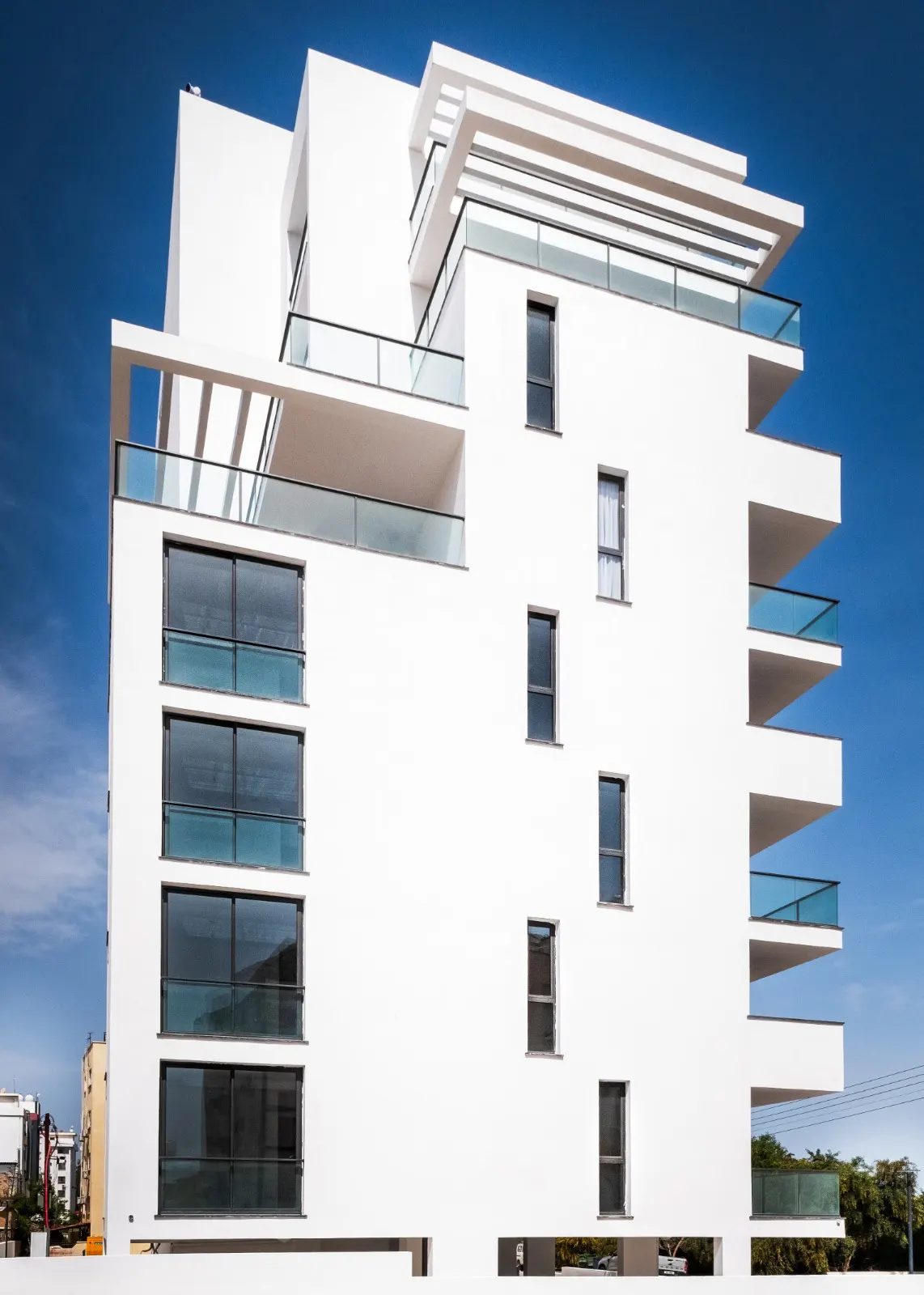 White apartment building with stacked terraces seen from street level